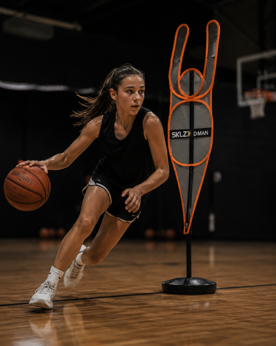 An athlete driving hard down the court, eyes up, reading the defense while dribbling past a training dummy.